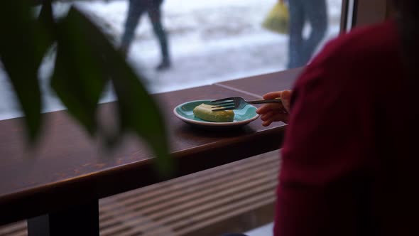 Woman Sits in Cafeteria Eats Dessert Looks Out the Window at People Passing By