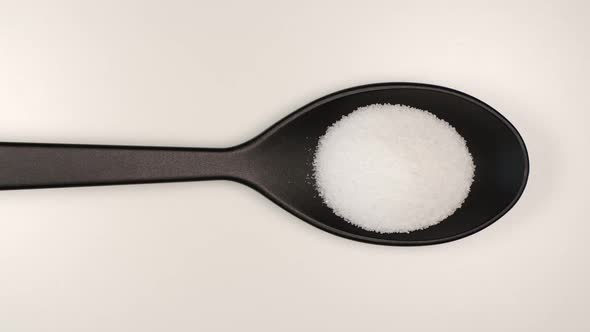  White salt fill a plastic spoon on a table