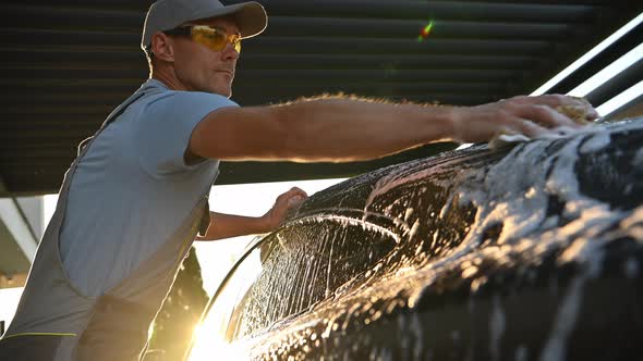 Men Washing His Car with a Sponge During Sunset alt