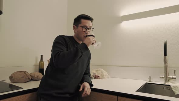 Asian man drinks wine in kitchen