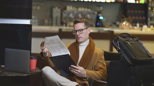 Portrait of Young Businessman Working on Laptop and with Documents in Hotel Lobby