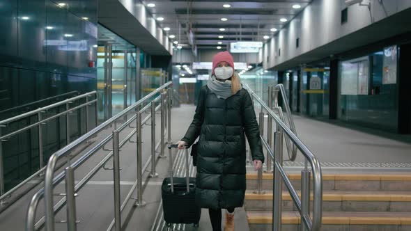 Coronavirus Travel Ban: Woman in Surgical Mask Walks with Suitcase in Airport