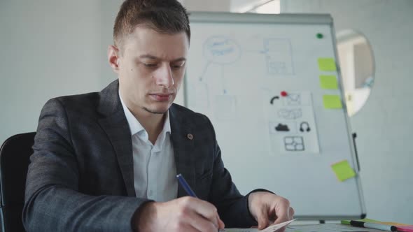 Young American Businessman Writing in Document Sitting at Table in Office