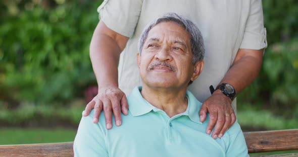 Video of happy biracial senior couple embracing and sitting on bench in garden alt