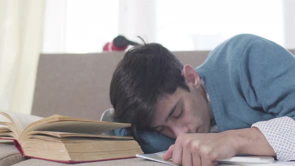 Close-up Portrait of Young Caucasian Boy Sleeping on Couch with Book and Tablet. Exhausted Male alt