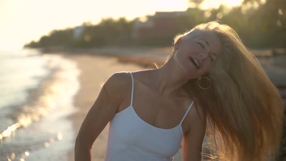 Slow motion of backlit mature woman on a beach shaking her hair to the right and smiling at the came alt