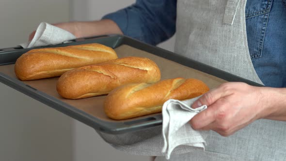 Hands Hold Baked French Baguette in Baking Sheet
