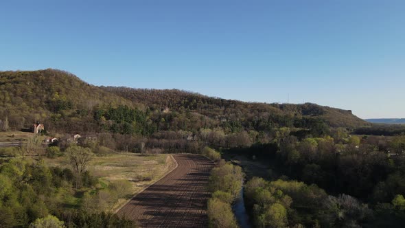 View of mountain with forest, farm field in the valley with a creek and open field with blue sky.