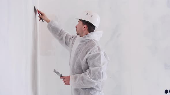 A Man in a Protective Suit Levels the Walls with a Spatula and Plaster