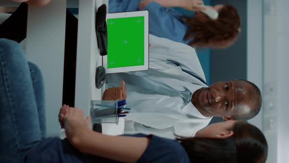 Vertical Video Tripod Shot of Pediatrician Showing Horizontal Green Screen on Tablet alt