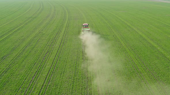 A red tractor against a background of a green field sprays mineral fertilizers. alt