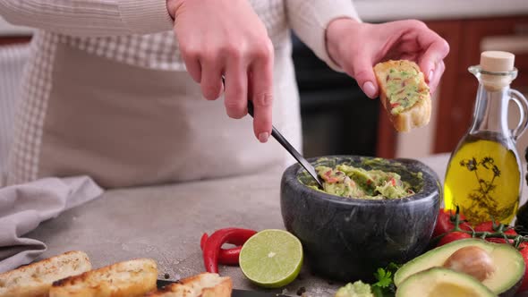 Woman Making Bruschetta with Freshly Made Guacamole Sauce at Domestic Kitchen alt