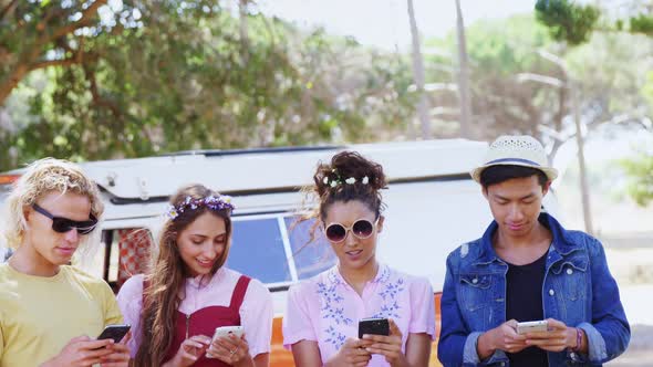 Friends using mobile phone near camper van in park 4k alt