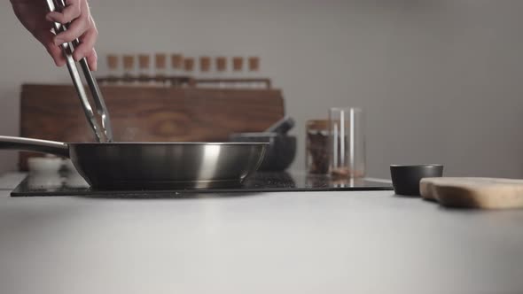 Man Flip Beef Steak with Tongs on Steel Pan on Electric Hob on Kitchen