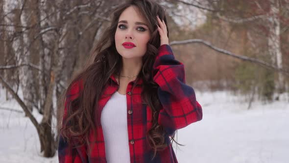 Young Woman with Wavy Hair Standing and Touching Face in Winter Forest