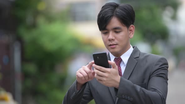 Young Handsome Asian Businessman Using Phone in the Streets Outdoors alt