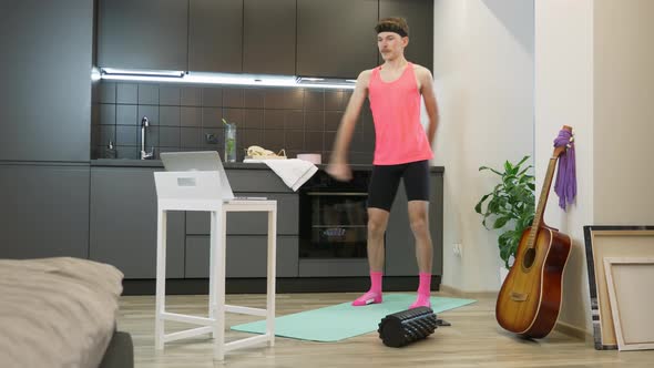 Fitness man in pink sportswear dancing enjoying music and warming up for workout in kitchen at home alt