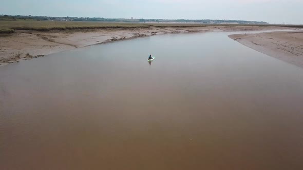 Man kayaking on meandering river, drone pans up to reveal beautiful landscape in the background. alt
