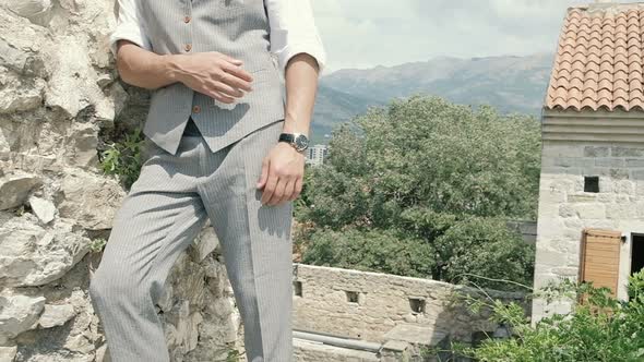 Attractive young fashion man in a suit walks around the old town along the plants. Slow motion alt