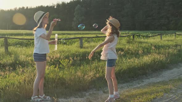 Children Blowing Soap Bubbles, Two Girls Playing in Nature alt