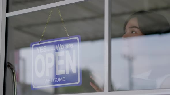 Asian woman business owner hanging close sign label on entrance glass door of coffee shop cafe alt