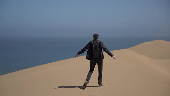 A Young Man Walks Along Sandy Dunes on the Seashore