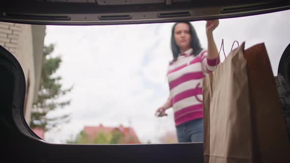 Caucasian Girl Opens the Trunk and Takes Away Shopping alt