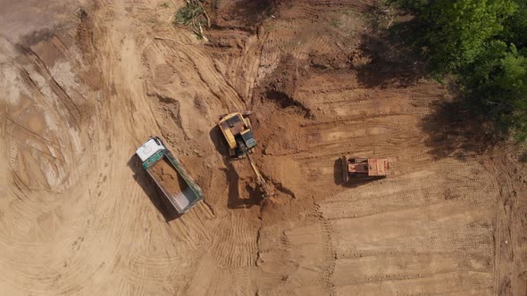 Aerial top view: yellow excavator pouring soil into tipper .