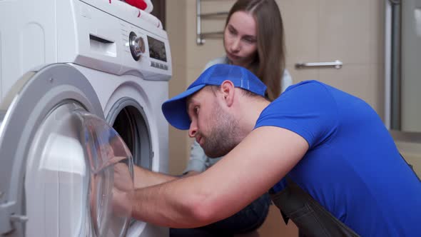 Repairman Repairs a Washing Machine in Front of a Woman alt