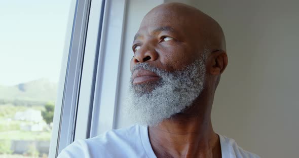 Side view of mature black man looking through window in a comfortable home 4k alt