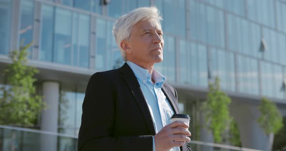 Medium Shot of Mature Smiling Businessman in Formal Wear Holding Coffeetogo Outside alt