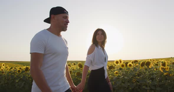 A Happy Couple Is Walking Through A Field Of Sunflowers