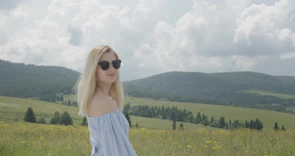 A Beautiful Girl Is Turning To the Camera. Smiling Girl. Sunny Day. Beautiful Mountains alt
