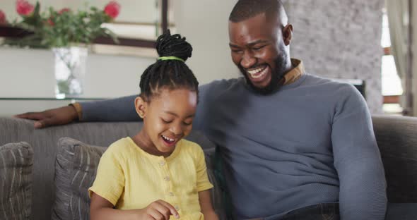 Happy african american daughter and father using tablet on sofa alt
