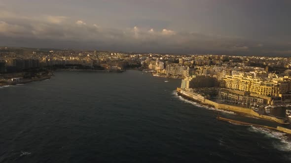 Wide aerial view of St. Julian, Malta at sunrise. A golden light shines on the buildings of the city alt