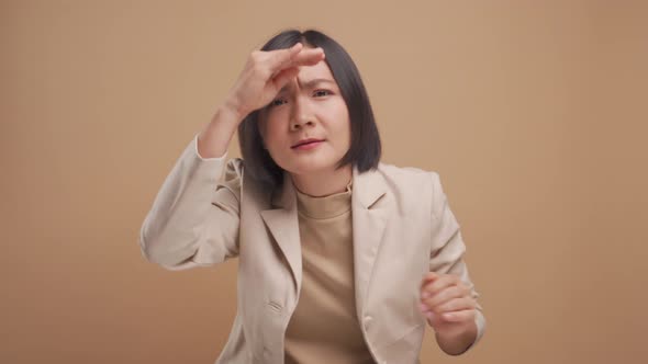 Asian business woman holding hand over eyes and peering attentively looking at camera isolated