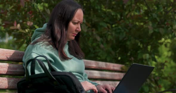 Woman Is Working On Laptop Sitting On Bench In Park Remote Work Concept