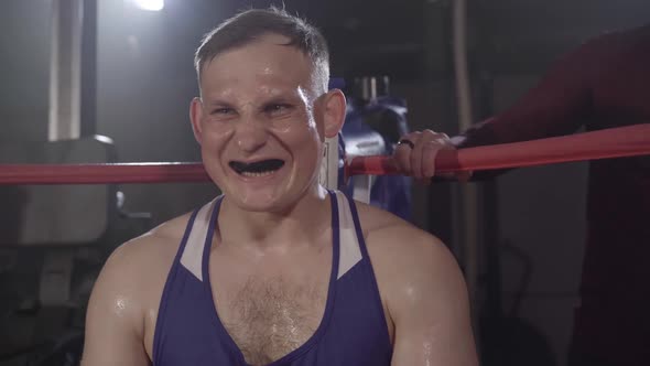 Coach Giving Kappa To Young Perspiring Boxer Sitting in Corner. Camera Approaches To Serious alt