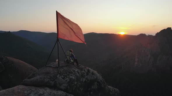 Aerial View of Young Travelers Father and His Two-year-old Son Sit on Top of a Mountain and Watch alt