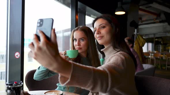Two Young Attractive Girls in a Cafe Take Selfies Smile and Pose
