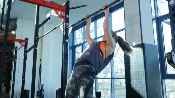 Athletic Young Woman Doing Pull-ups on a Horizontal Bar at Fitness Gym