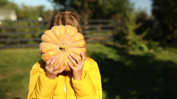 Happy child girl covers the face with pumpkin outdoors in halloween
