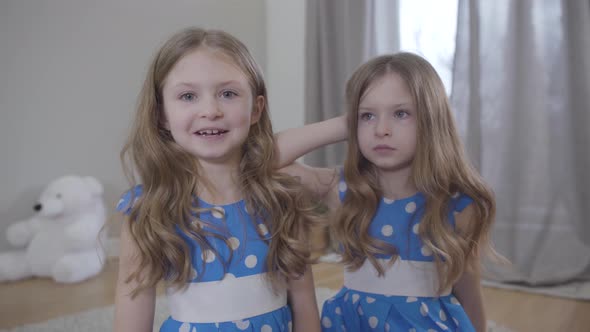 Happy and Sad Caucasian Twins Talking Indoors. Portrait of Joyful Girl and Upset Child at Home alt