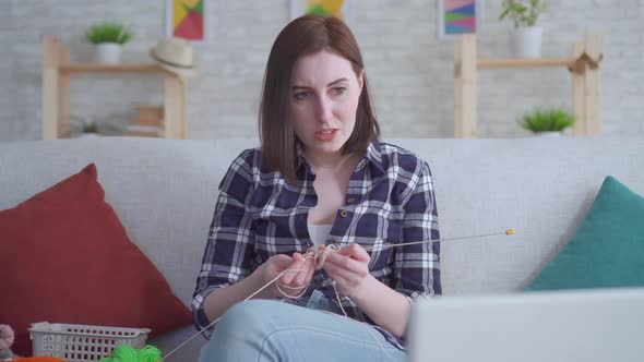 Woman Sitting in Front of a Laptop and Watching a Video Tutorial on Knitting and It Does Not Work alt