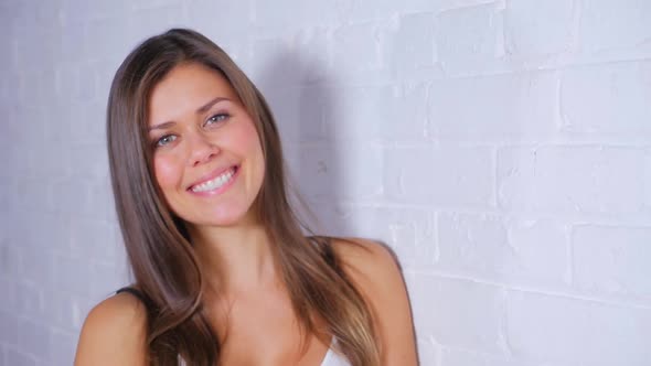 Young Attractive Female Turning To Camera And Smiling While Leaning Against A White Brick Wall 2