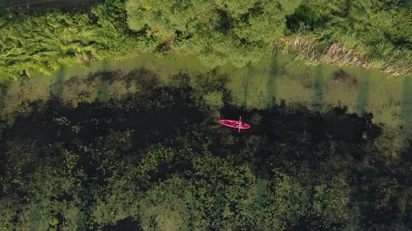 Girl traveller is exploring river in kayak at sunset, drone top view. Water travelling. Top view alt