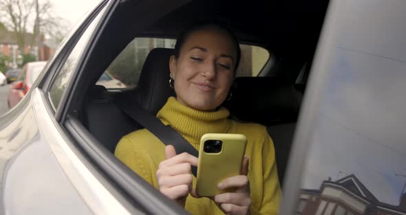 Happy woman sitting on taxi car back seat, using the phone and smiling