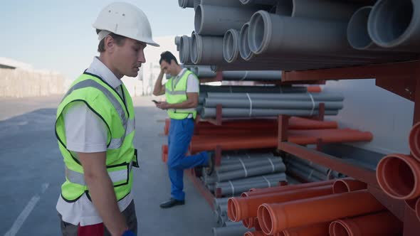 Dissatisfied Caucasian Warehouse Worker Looking at Lazy Middle Eastern Coworker Surfing Internet on alt