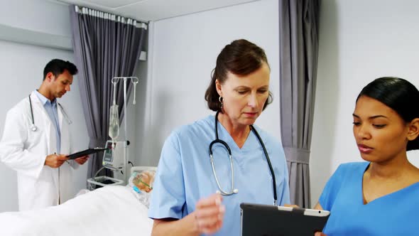 Nurses discussing over digital tablet while doctor checking a iv drip on patient alt