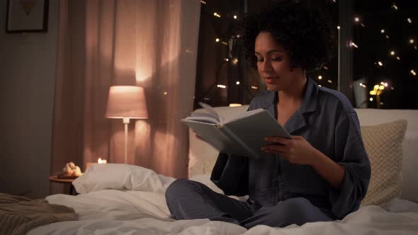 Woman in Pajamas Reading Book in Bed at Home